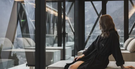 The best references for our hotel marketing Woman in bathrobe sitting on sofa looking out large windows at mountain landscape