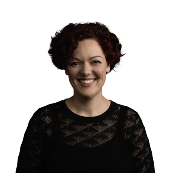 Victoria Morandell | Senior Copywriter Porträt einer lächelnden Frau mit kurzen lockigen roten Haaren und schwarzem Spitzenoberteil