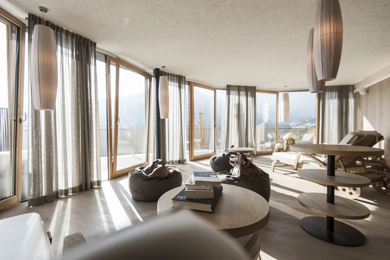 Eine Website mit Stil – made by Brandnamic Heller Wohnzimmerbereich mit großen Fenstern, Vorhängen, Sitzsäcken und Holzmöbeln