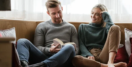 The best references for our hotel marketing Couple sitting on couch, man reading a book, woman smiling and listening