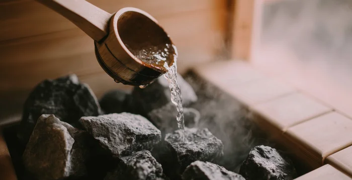 Marketing per hotel – la vostra agenzia di marketing per hotel in Alto Adige Acqua versata con mestolo di legno su pietre calde nella sauna