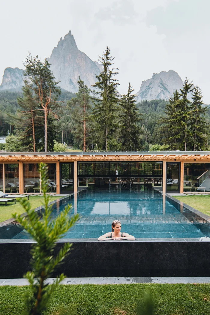 Brandnamic: Hotellösungen von Hospitality-Experten Frau entspannt in einem Pool vor Bergen und Bäumen im Hintergrund