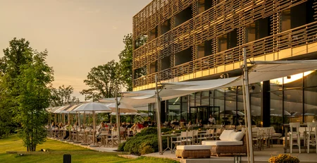 The best references for our hotel marketing Outdoor restaurant with tables and umbrellas next to modern building at sunset