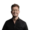 Alles Interessante rund um Online-Marketing für Hotels Mann mit Brille und schwarzem Hemd lächelt vor weißem Hintergrund