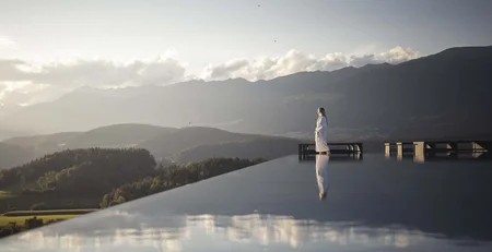 Die besten Referenzen für unser Hotelmarketing Person in Bademantel am Infinity-Pool mit Berglandschaft im Hintergrund