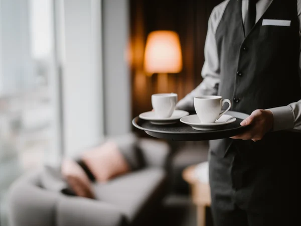 Marketing für Hotels – eure Hotelmarketing-Agentur aus Südtirol Kellner trägt zwei Tassen Kaffee auf Tablett in gemütlichem Hotelzimmer