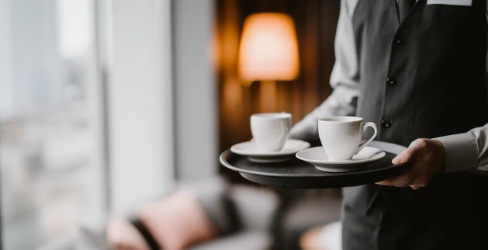 Marketing per hotel – la vostra agenzia di marketing per hotel in Alto Adige Cameriere che porta due tazze di caffè su un vassoio in una stanza d'hotel accogliente