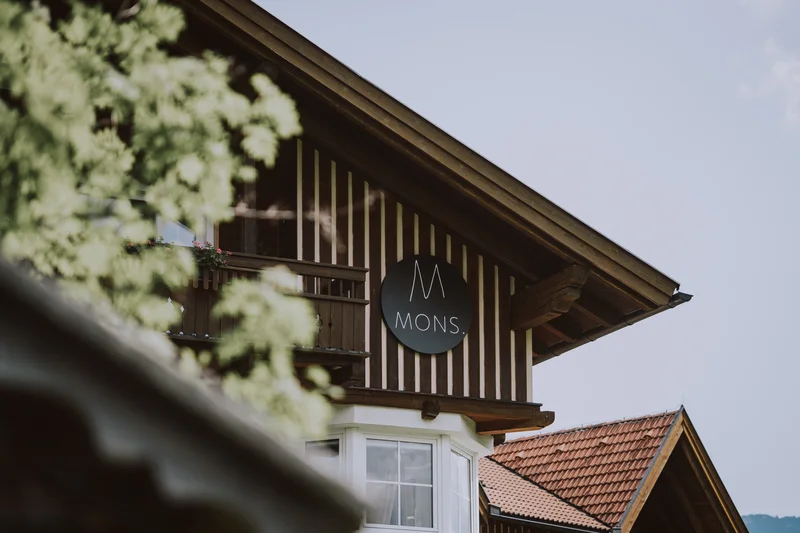 Wein, Hotel und Marketing – ein leckeres Trio Fassade eines Holzzaunhauses mit MONS Schild