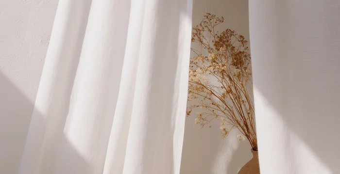 Hotelberatung: Experten für die Hospitalitybranche Trockenblumen in Vase hinter weißen Vorhängen mit Sonnenlicht