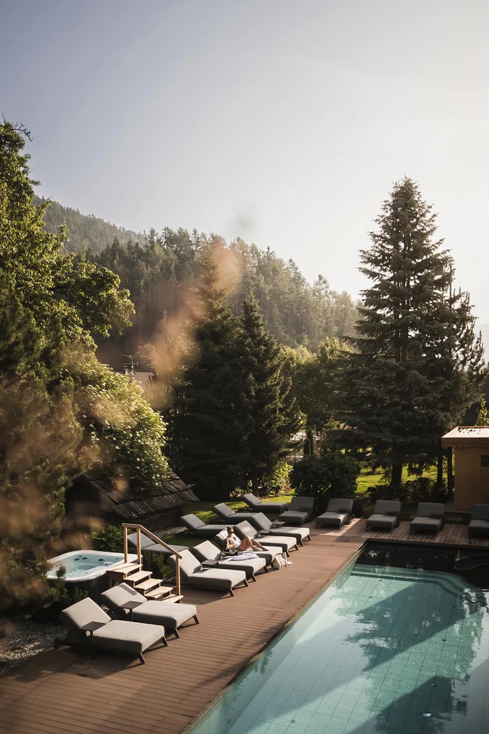 Brandnamic: Hotellösungen von Hospitality-Experten Frau entspannt auf Liegestuhl neben Pool und Jacuzzi in sonniger Gartenanlage