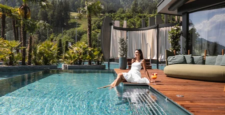The best references for our hotel marketing Woman in white dress relaxing by pool with mountains and palm trees in background