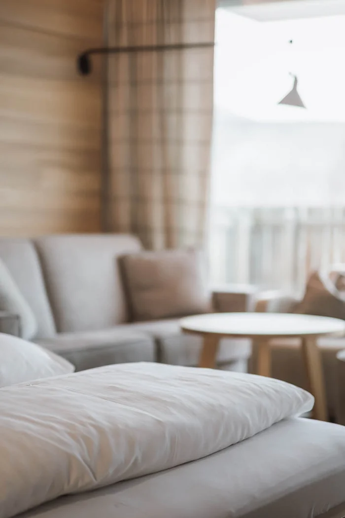 Brandnamic: Hotellösungen von Hospitality-Experten Nahaufnahme weißen Kissens auf Bett in gemütlichem Wohnzimmer mit Sofa und Tisch