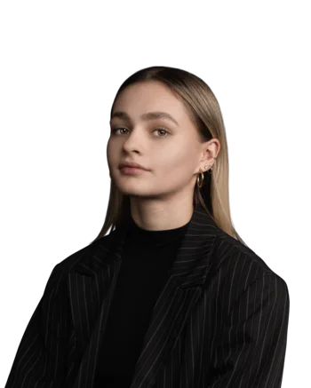 Lea Blasbichler | Senior Content Manager Junge Frau mit hellem Haar und gestreiftem schwarzen Blazer vor weißem Hintergrund