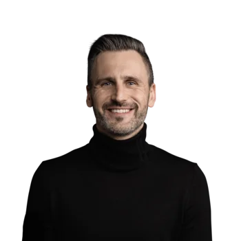 Oliver Schenk | Head of Operations Lächelnder Mann mit schwarzen Pullover und kurzem Haar vor weißem Hintergrund