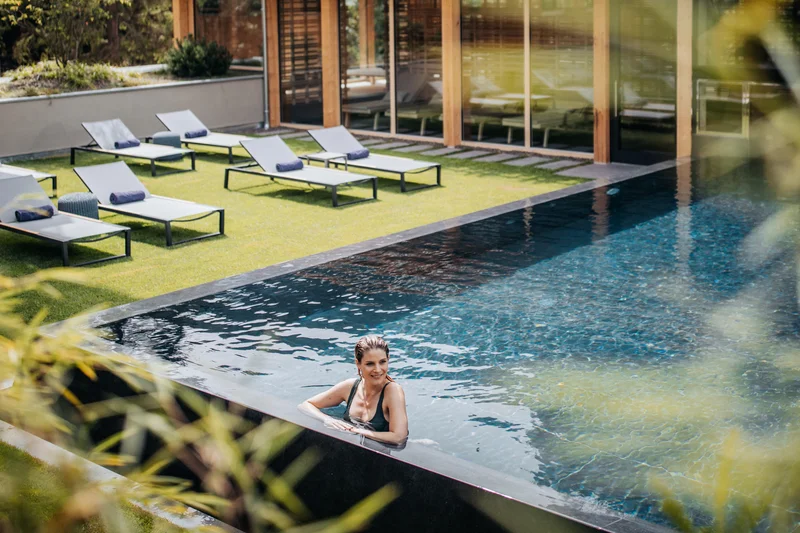 Erfolgreiches Marketing aus Brixen Frau im Pool mit Liegestühlen und Holzhaus im Hintergrund