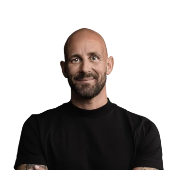 Hannes Gasser | CRO Porträt eines lächelnden, tätowierten Mannes mit schwarzem T-Shirt vor weißem Hintergrund