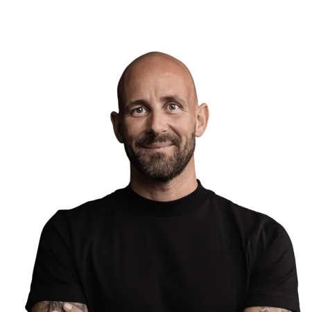 Brandnamic: Hotellösungen von Hospitality-Experten Porträt eines lächelnden, tätowierten Mannes mit schwarzem T-Shirt vor weißem Hintergrund