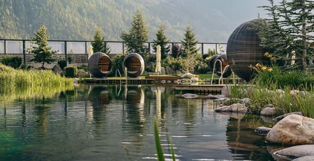 Die besten Referenzen für unser Hotelmarketing Natürlicher Schwimmteich mit modernen Sitzkapseln und Bergkulisse