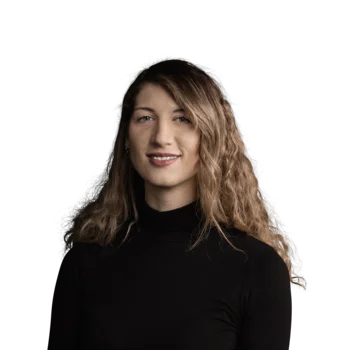 Irene Ferrara | Senior Copywriter & Translator Portrait einer lächelnden Frau mit lockigem Haar und schwarzem Rollkragenpullover