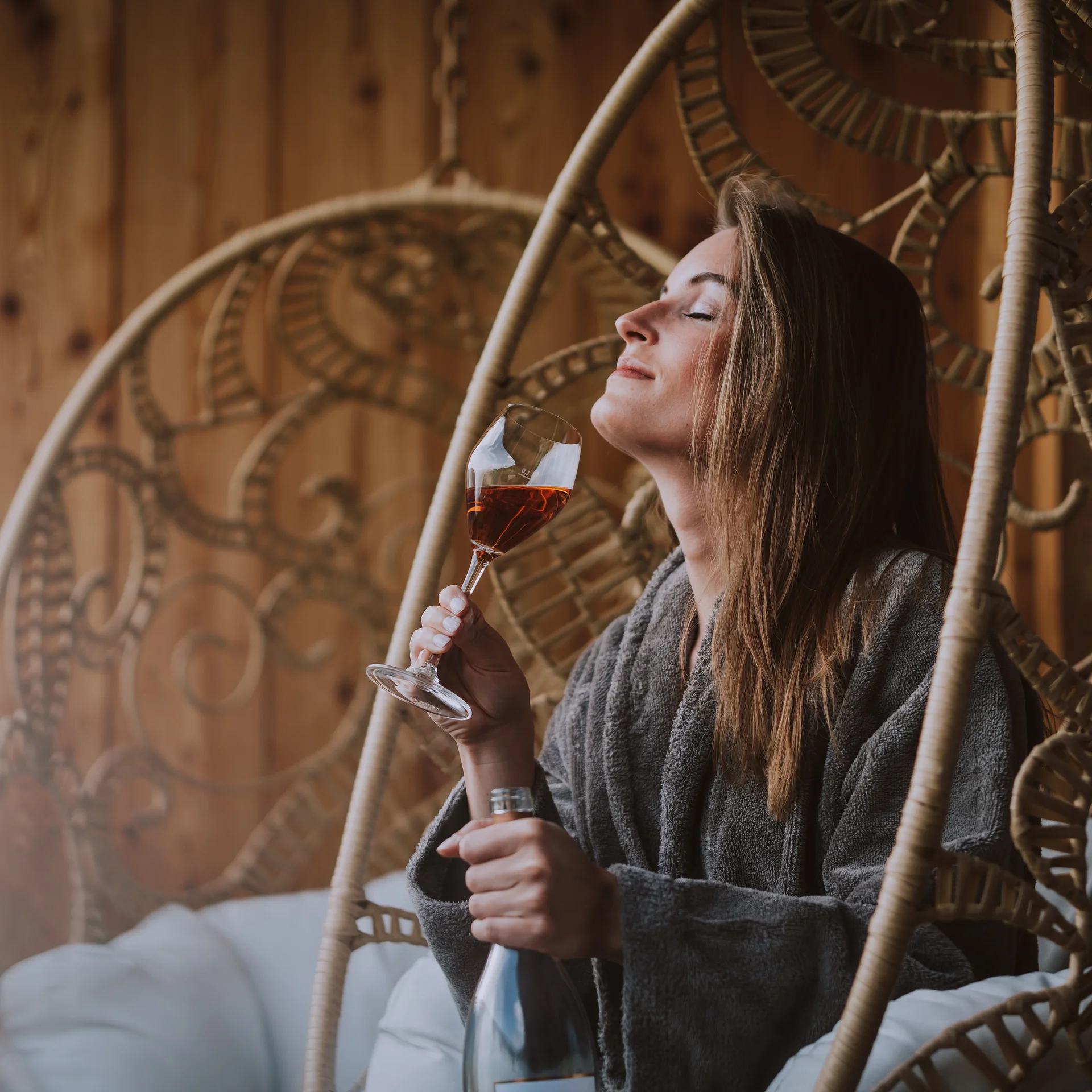 Wein, Hotel und Marketing – ein leckeres Trio Frau entspannt in Hängesessel mit Weinglas und Flasche in Holzinterieur