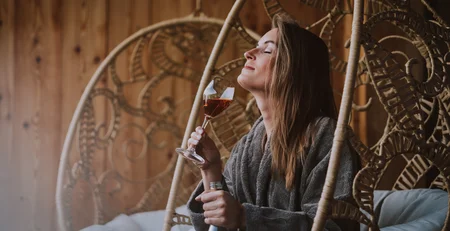 The best references for our hotel marketing Woman relaxing in hanging chair with wine glass and bottle in wooden interior