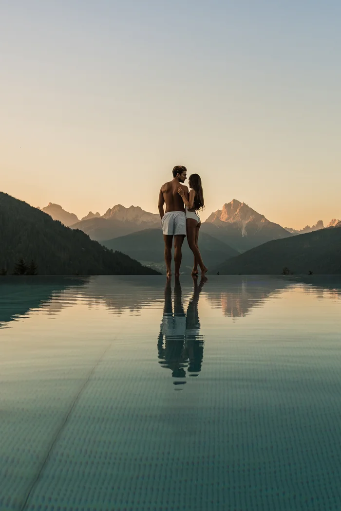 Brandnamic: Hotellösungen von Hospitality-Experten Paar in Badebekleidung am Infinity-Pool mit Bergblick im Sonnenuntergang
