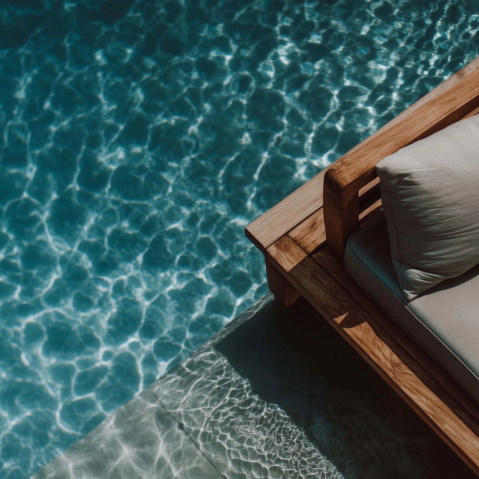 Eure Agentur für die ideale Positionierung Holzliege mit Kissen am Rand eines Pools mit klarem blauem Wasser