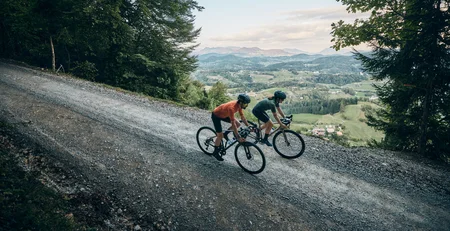 The best references for our hotel marketing Two cyclists riding on a gravel road in a hilly, forested landscape